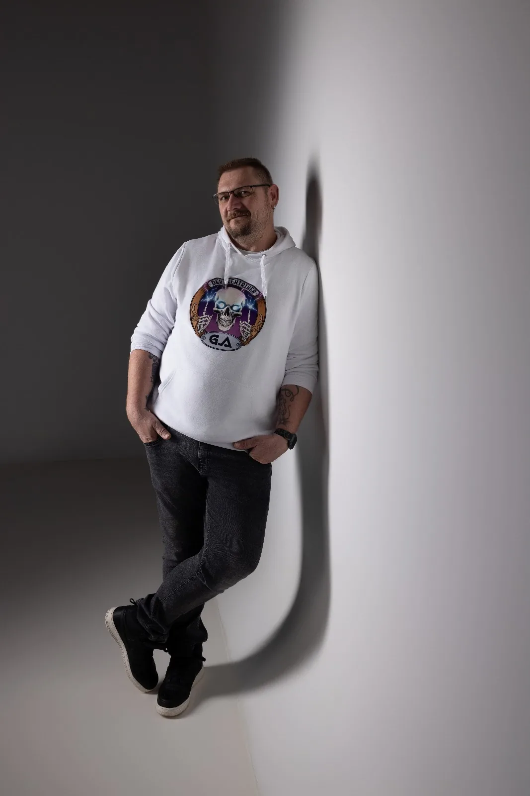 Gerhard Atzberger lehnt im Hoodie mit seinem Logo an einer weißen Wand